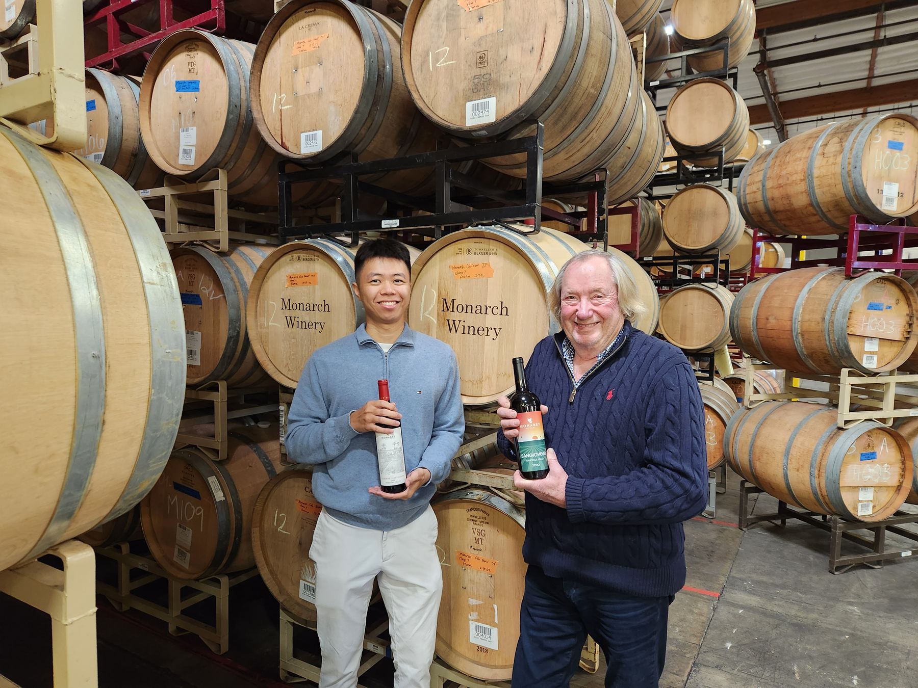 Two men holding bottles of Monarey wine in the barrel room